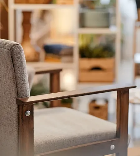 Nahaufnahme eines gemütlichen Polstersessels mit Holzlehnen in einem wohnlich eingerichteten Zimmer mit einem Bücherregal im Hintergrund.