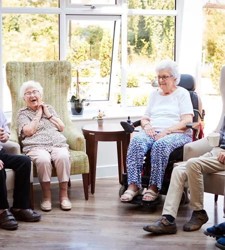 Ältere Frauen und Männer sitzen in bequemen Sesseln in einem Aufenthaltsraum und verbringen Zeit miteinander.