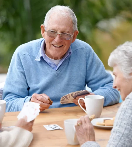 Ältere Menschen spielen Karten an einem Tisch und trinken Kaffee.